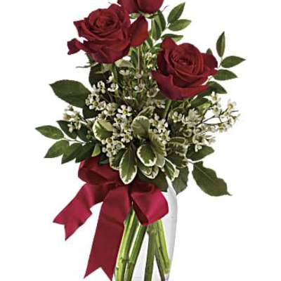 Red roses in a clear glass vase with a burgundy ribbon