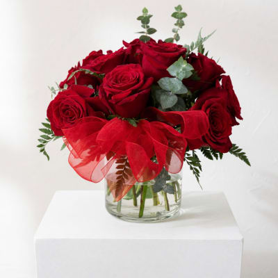 Red roses in a clear glass vase with a red ribbon bow