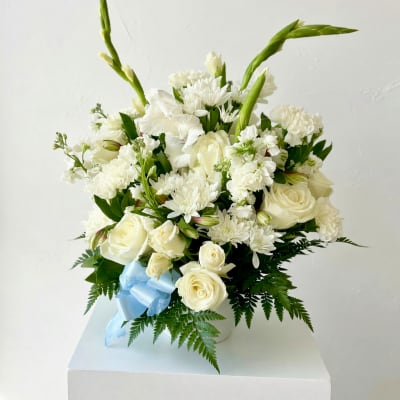 White roses and chrysanthemums arranged in a vase with a blue ribbon
