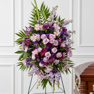 Large purple and pink floral standing spray beside a casket