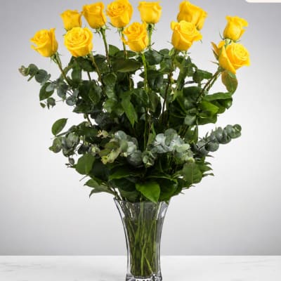 Yellow roses in a clear glass vase with mixed greenery