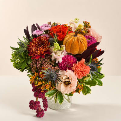 Autumn bouquet with mixed flowers and a small pumpkin in a clear glass vase
