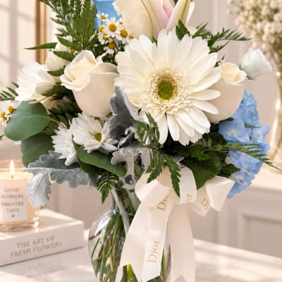 Bouquet of white daisies, roses, and blue hydrangeas in a glass vase
