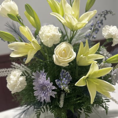 Bouquet of pale yellow lilies, white carnations, and lavender flowers in a vase