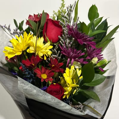 Bouquet of red roses, yellow daisies, and purple flowers wrapped in paper
