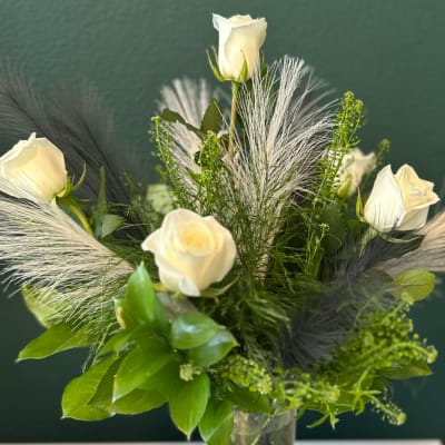 White roses arranged in a clear vase with feathery accents