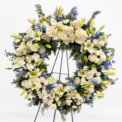 Large white floral wreath on a black stand with cream and blue flowers