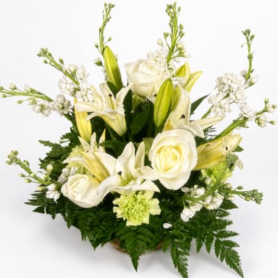 White roses and lilies arranged in a low basket with white filler flowers