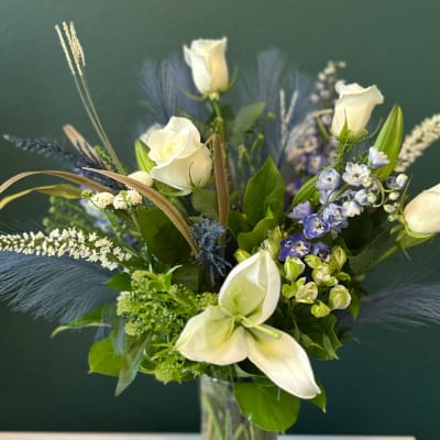 White roses and calla lilies in a glass vase with blue accents