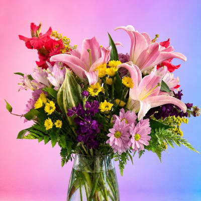 Mixed bouquet of pink lilies, daisies, and purple flowers in a glass vase