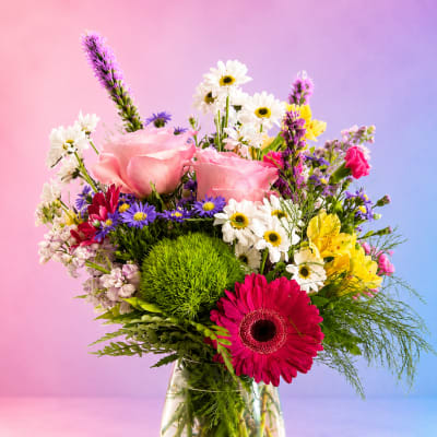 Mixed bouquet of pink roses, daisies, and gerbera in a clear glass vase