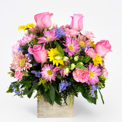 Mixed pink and yellow flowers arranged in a square wooden container