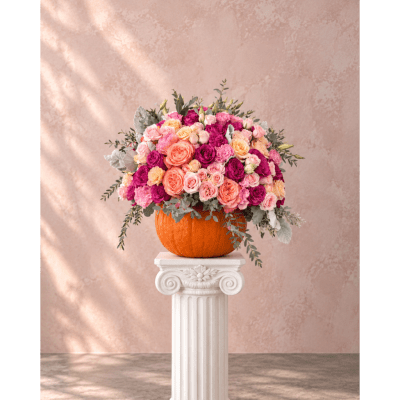 Pink and peach rose arrangement in a pumpkin vase on a white pedestal