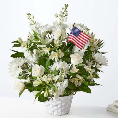 White floral arrangement in a white basket with a small American flag