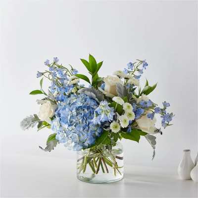 Blue hydrangeas and white roses in a clear glass vase