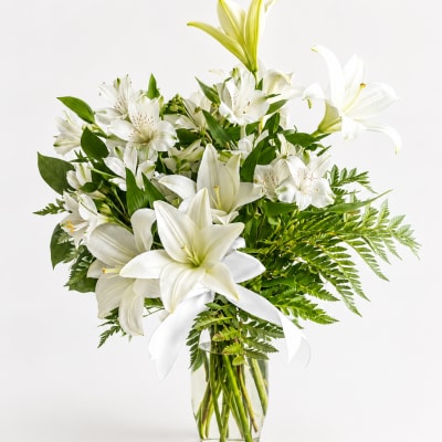 White lilies and alstroemeria in a clear glass vase with a white ribbon