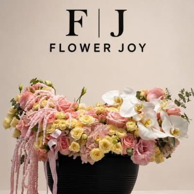 Pink and yellow floral arrangement in a black vase with white orchids
