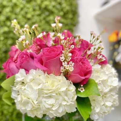 Low round arrangement of hot pink roses and white hydrangeas in a green-accented glass bowl vase