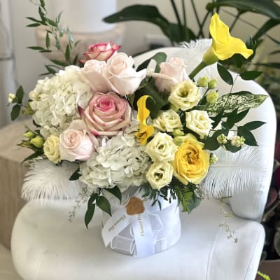 Bouquet of pale roses, white hydrangeas, and yellow calla lilies in a white box