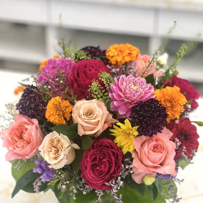 Mixed bouquet of roses, dahlias, and marigolds in a square glass vase