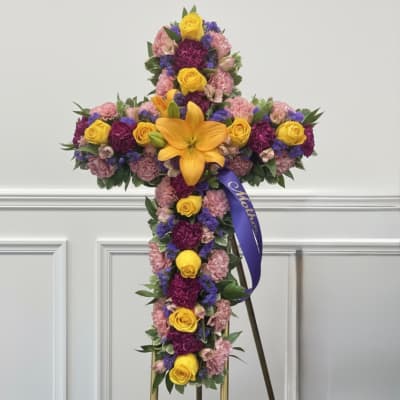 Cross-shaped floral tribute with yellow roses, lilies, and pink and purple flowers