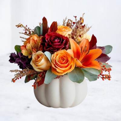 Autumn bouquet of orange, red, and cream roses in a white pumpkin vase
