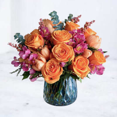 Orange roses and pink flowers arranged in a blue glass vase