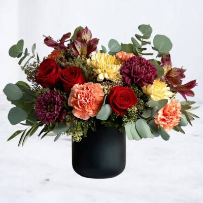 Mixed bouquet of red roses, carnations, and chrysanthemums in a black vase