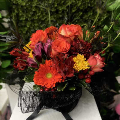 Compact arrangement of red and orange roses, gerbera daisy, and mixed blooms with black mesh wrap