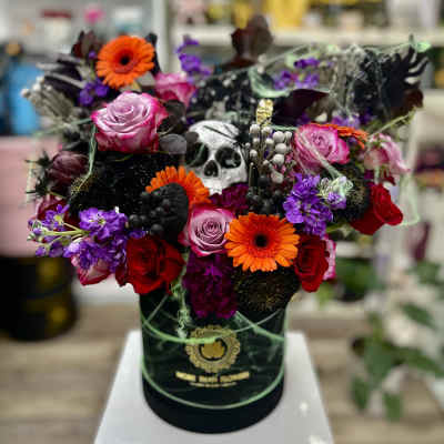 Halloween flower hatbox with bright roses, gerberas, purple blooms and a skull decoration.