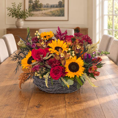 Mixed bouquet with sunflowers, red roses, and orchids in a gray basket