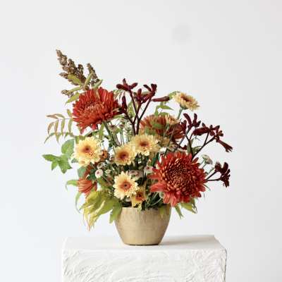 Autumn flower arrangement in a gold vase with red and cream blooms
