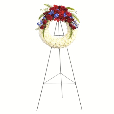 Standing funeral wreath with red roses, white flowers, and blue accents on an easel