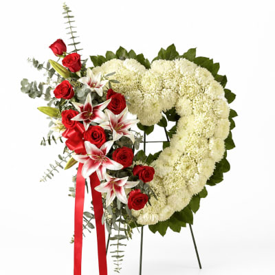 Heart-shaped floral wreath with white chrysanthemums, red roses, and lilies on a stand