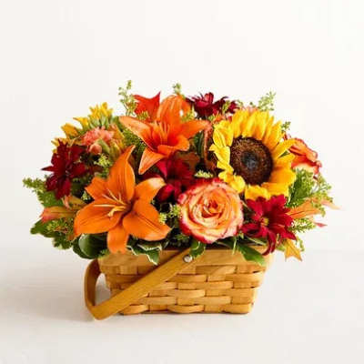 Basket of orange lilies, yellow sunflower, red blooms, and roses in a woven basket.