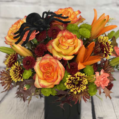 Orange roses and mixed mums in a black vase with a decorative spider accent