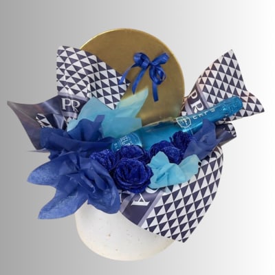 Blue gift arrangement with a champagne bottle, roses, and patterned wrap in a white container
