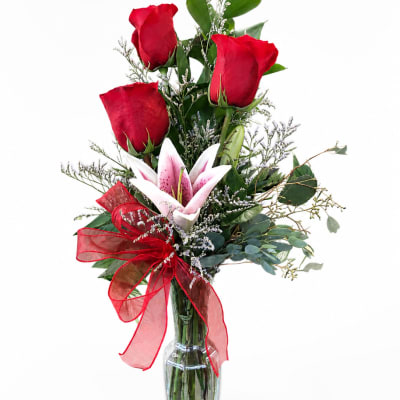 Red roses and a pink lily in a glass vase with a red ribbon