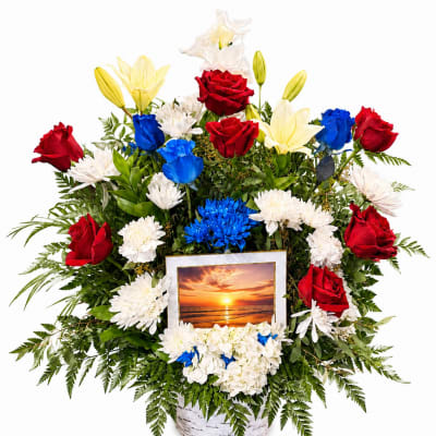 Basket arrangement of red, white, yellow, and blue flowers with a sunset photo