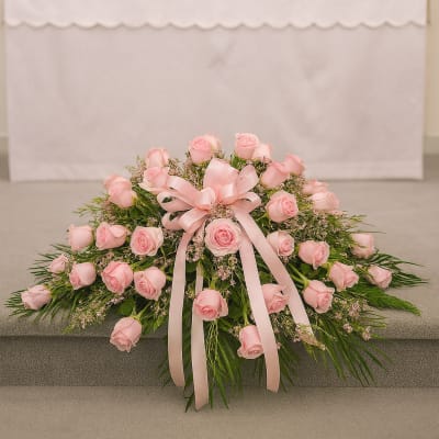 Pink rose casket spray with a satin ribbon in a church setting