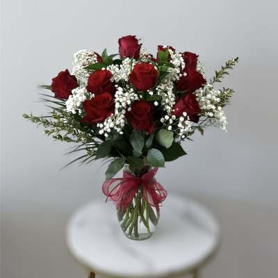 Clear glass vase of red roses with white filler flowers and a red bow.