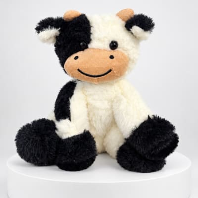 Black-and-white plush cow sitting on a white pedestal