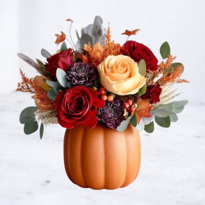 Fall bouquet in a pumpkin-shaped vase with red, peach, and purple flowers