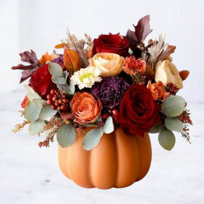 Fall floral arrangement in a pumpkin-shaped container with red and peach roses