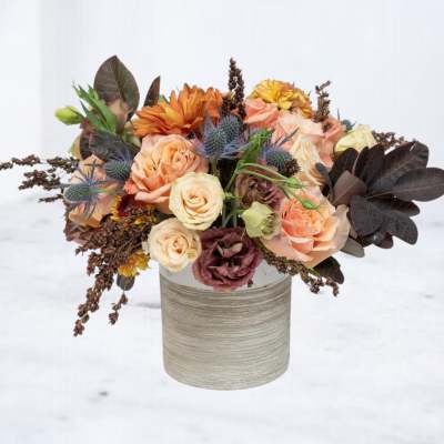 Peach and orange roses with mixed blooms in a cylindrical vase