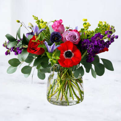 Mixed bouquet of red, pink, purple, and yellow flowers in a clear glass vase