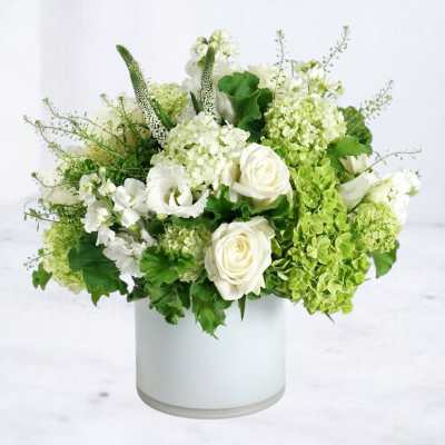 White and green floral arrangement in a white cylindrical vase