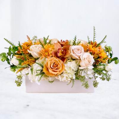 Low floral arrangement in a white rectangular box with peach, white, and orange blooms