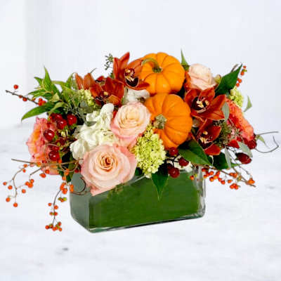 Autumn floral arrangement with pumpkins and roses in a glass vase