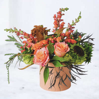 Peach roses and orange snapdragons in a round vase with mixed foliage